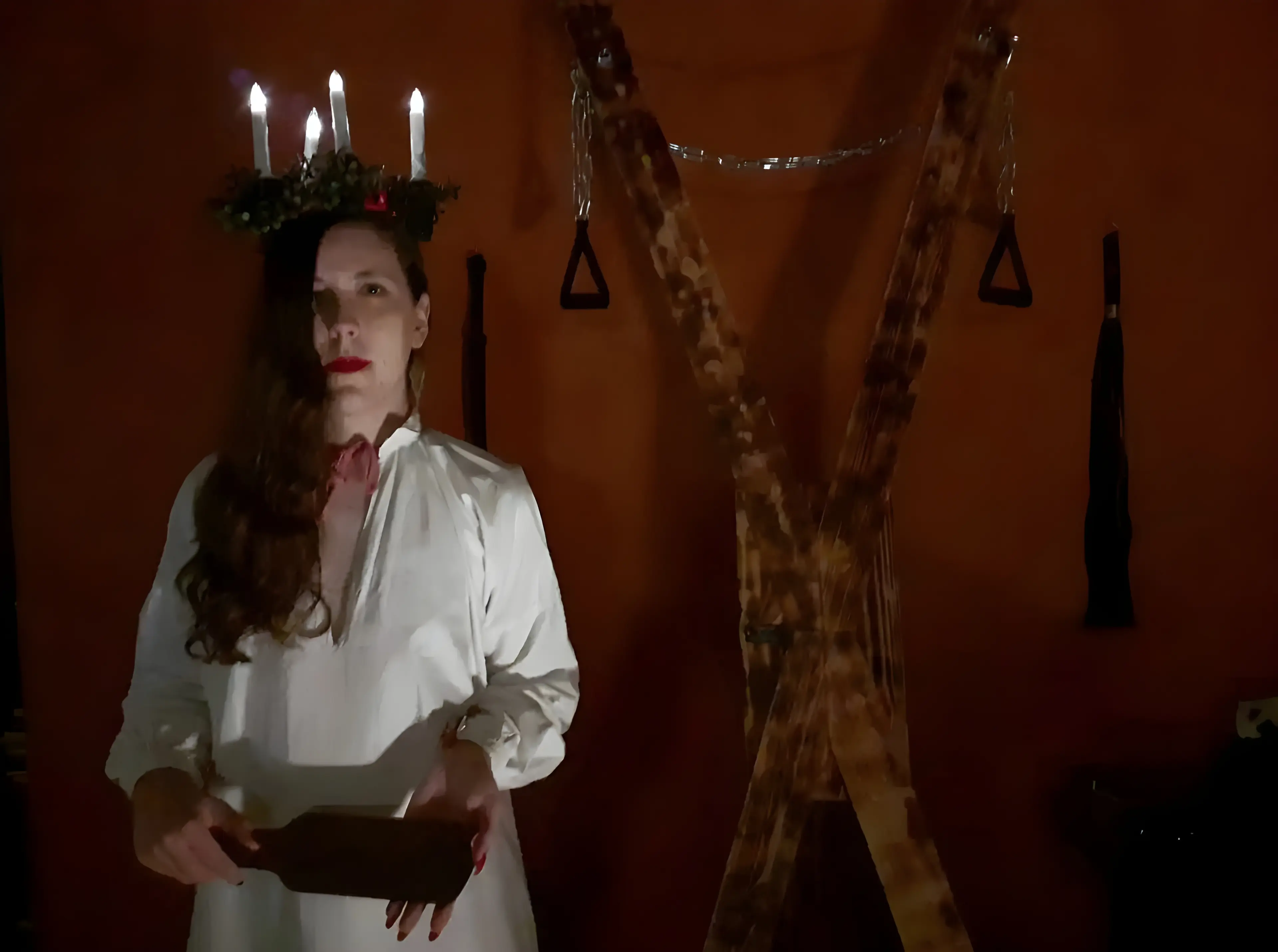 Gabrielle, en tenue traditionnelle de Sainte Lucie, mêlée à des éléments BDSM comme un paddle et une croix de Saint André